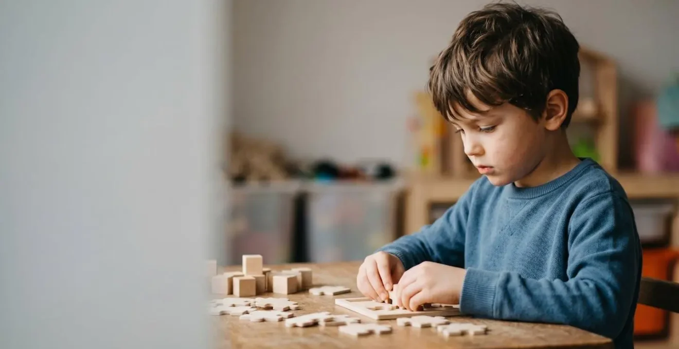 A young child sitting at a desk with focused expression while subtle environmental distractions fade into soft background blur